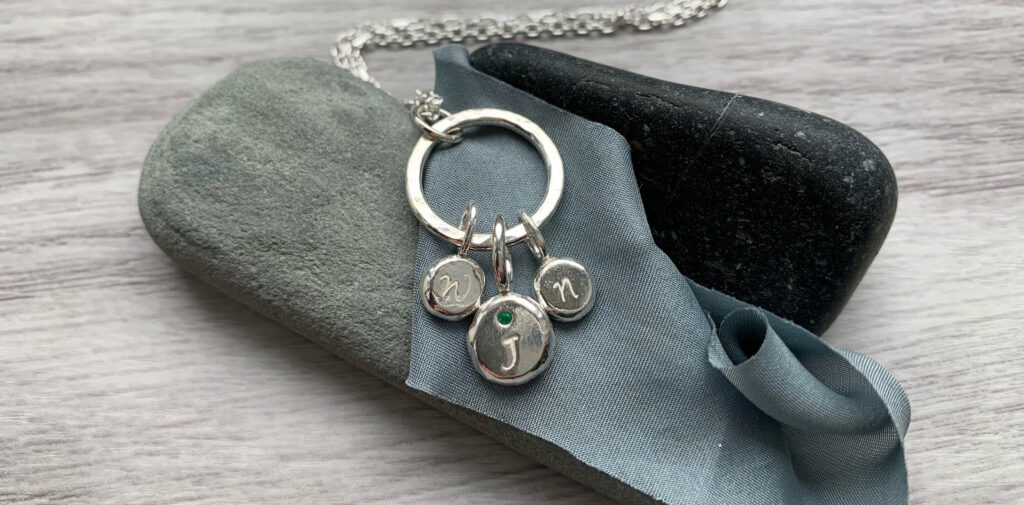 Handmade personalised pendant. Silver circle with three personalised pebbles using birthstone and initials.